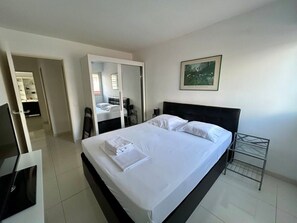 A modern hotel room with a large bed, a bedside table, a chair, a desk, a mirror, and a framed picture on the wall. - A007 - Appartement chic au coeur de Cannes (Cannes)