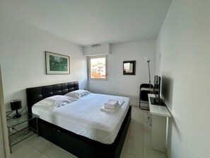 Een hotelkamer met een bed, nachtkastje, lamp, televisie en raam.