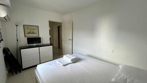 Hotellihuone, jossa on sänky, työpöytä, tietokone, tuoli ja naulakko.