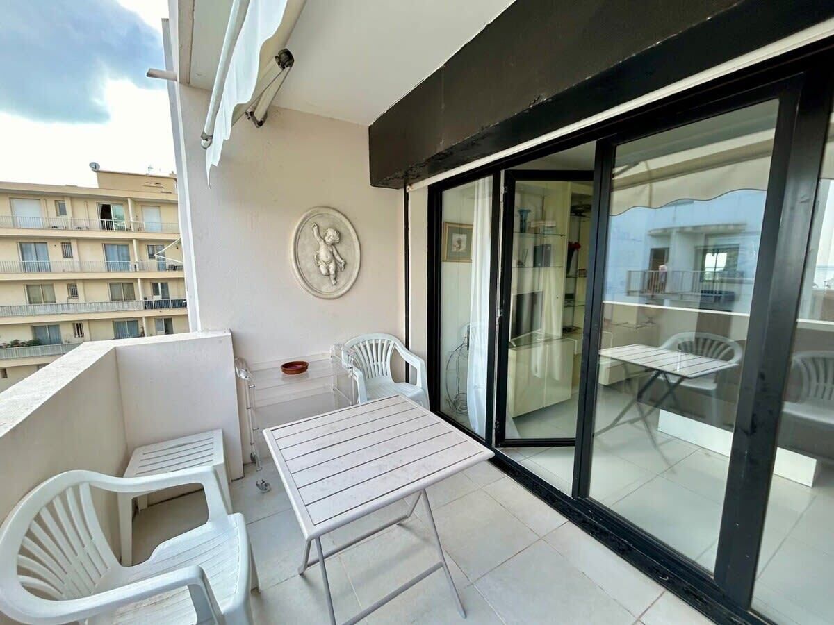 A balcony with a table and chairs, a decorative plate on the wall, and a view of the building across the street.