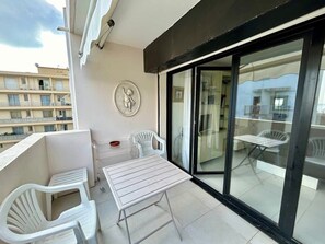 A balcony with a table and chairs, a decorative plate on the wall, and a view of the building across the street. - A007 - Appartement chic au coeur de Cannes (Cannes)