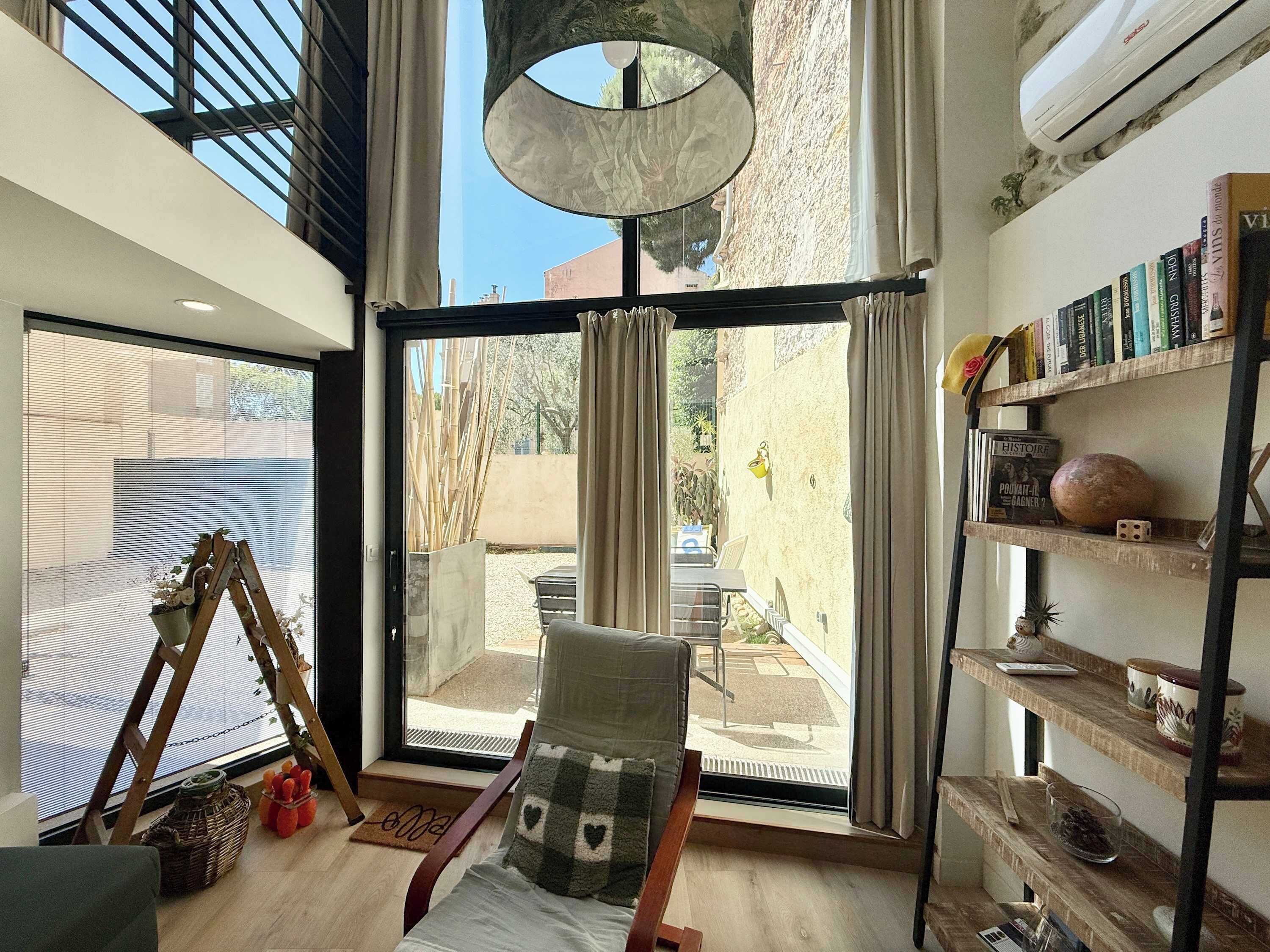 Ein Zimmer mit großem Fenster, einem Sessel, einem Bücherregal und einer Pendelleuchte.