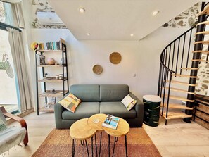 A living room with a grey sofa, two round wooden coffee tables, a bookshelf, a woven wall hanging, and a staircase with a wooden railing. - A088 Élégant duplex avec terrasse, plages, centre (Cannes)