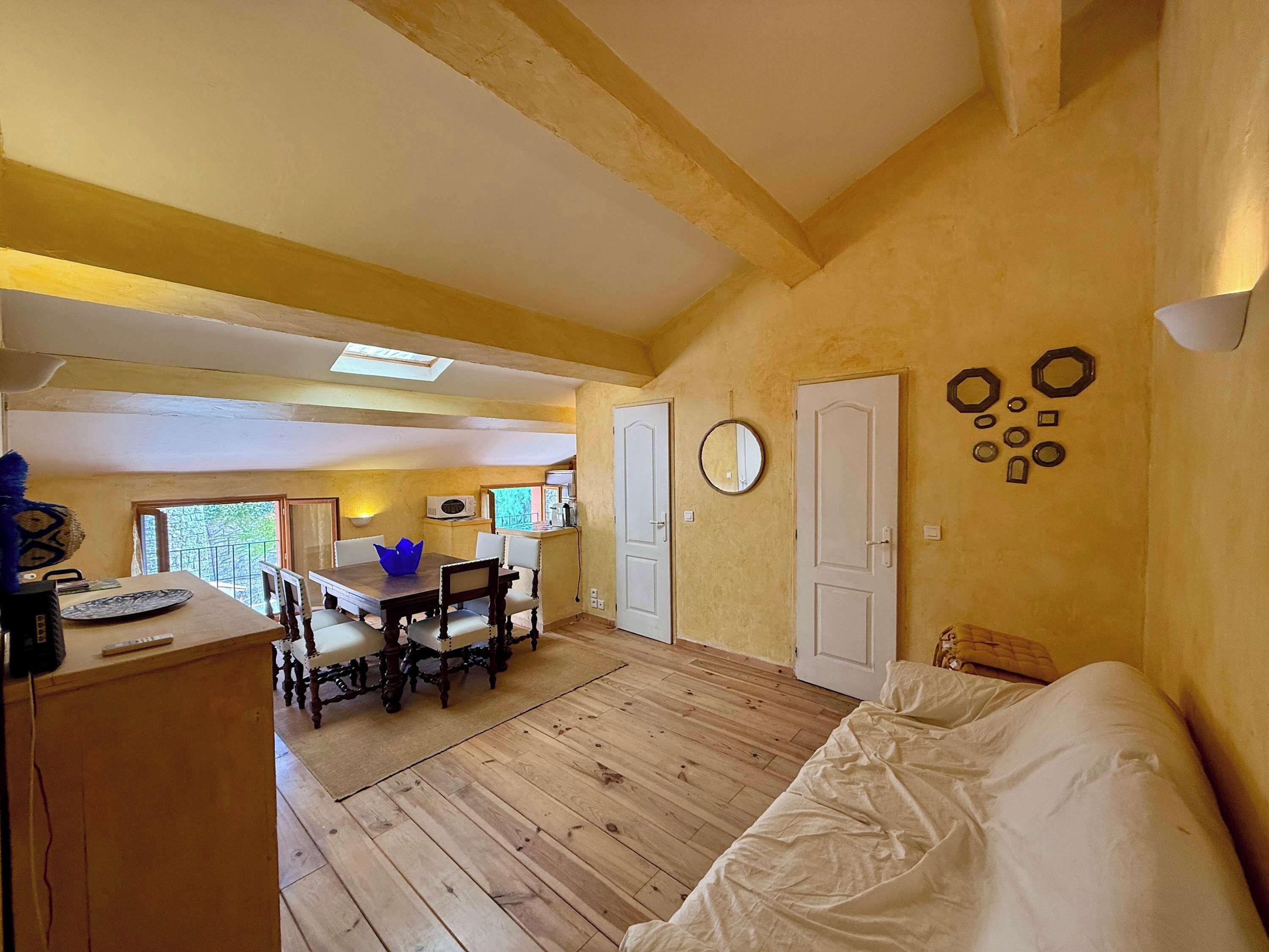 Une pièce avec un plancher en bois, un lit, une table à manger avec des chaises et un coin cuisine avec une fenêtre.