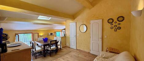 Une pièce avec un plancher en bois, un lit, une table à manger avec des chaises et un coin cuisine avec une fenêtre.