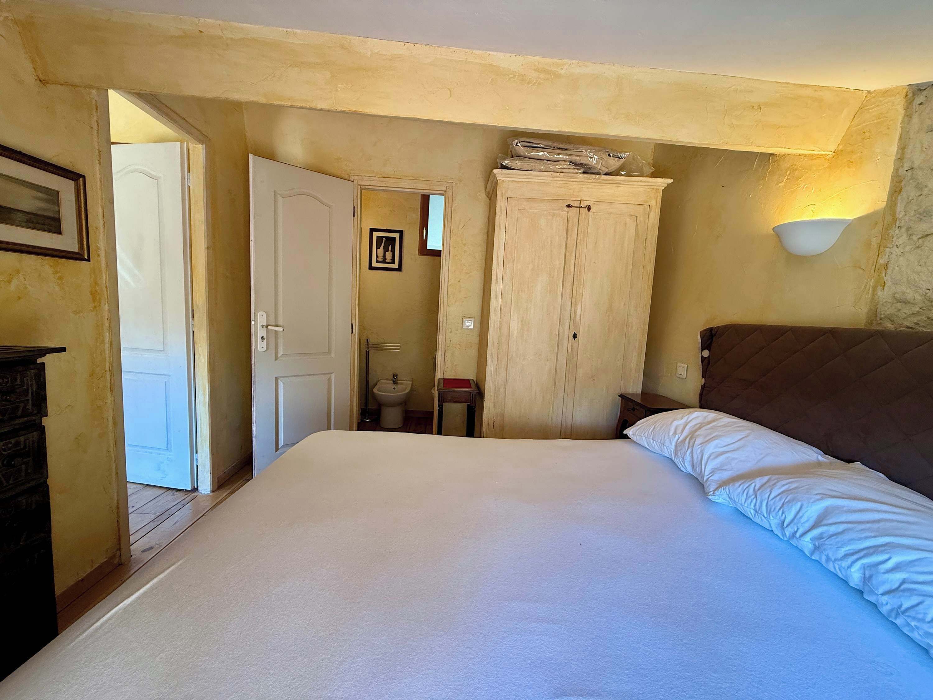 A bedroom with a bed, a wardrobe, a bedside table, and a wall-mounted light fixture.