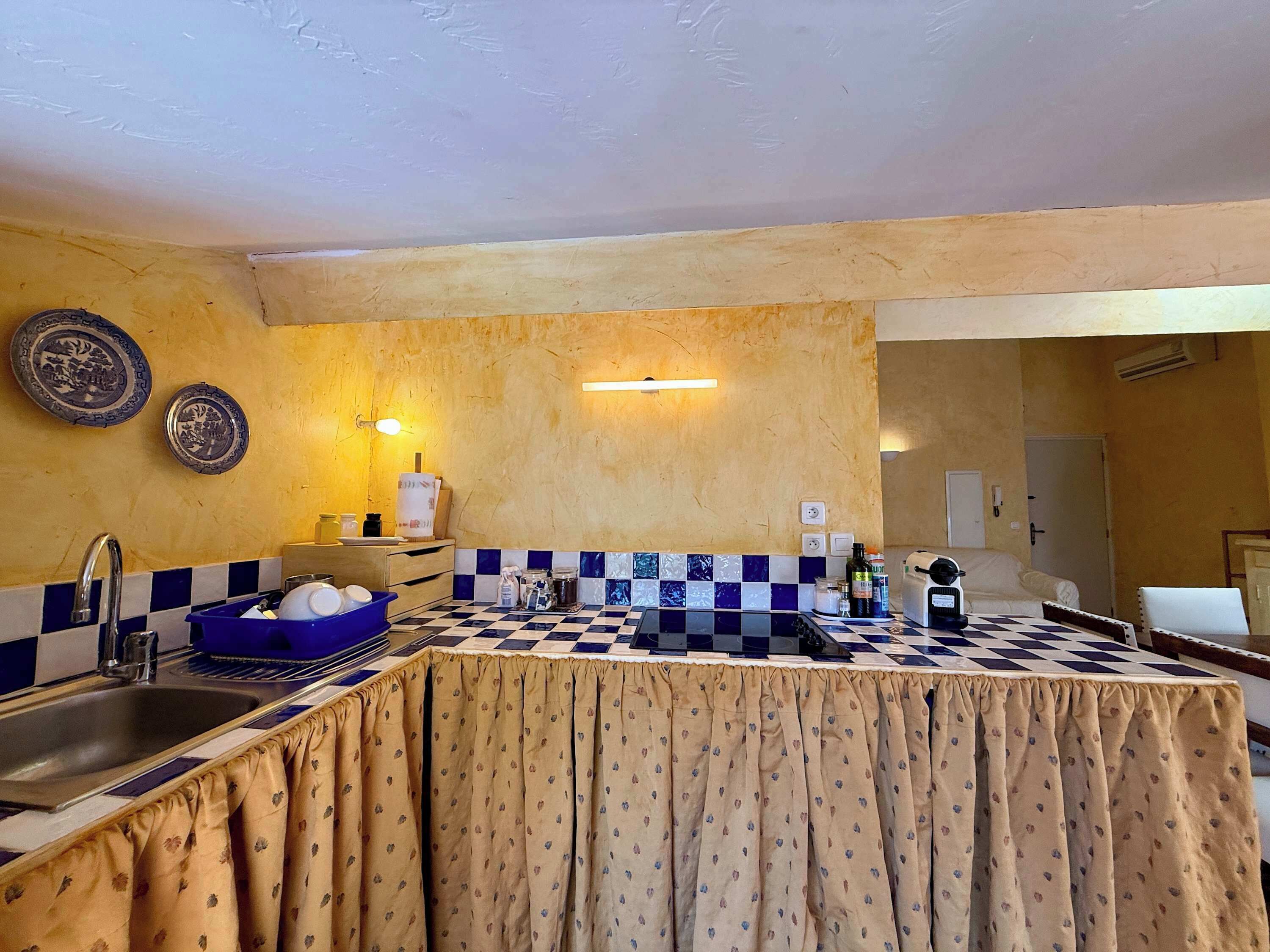 A kitchen with a checkered tile backsplash, a sink, and a countertop with a patterned tablecloth.