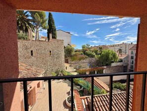 Ein Balkon mit Steinmauer, Blick auf einen Innenhof mit Terrakotta-Dächern und Gebäuden im Hintergrund.