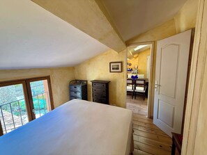 A bedroom with a large bed, a wooden floor, a door, and a view of a dining area. - A035 Bel appartement atypique Suquet (Cannes)