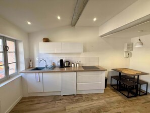 Eine moderne Küche mit weißen Schränken, einer Holzausziehtheke, einer Spüle, einer Kaffeemaschine und einem kleinen Esstisch mit Bänken.