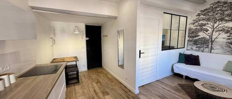 A modern kitchen with a built-in stove, a dining area with a wooden table, and a living space with a sofa and a wall-mounted TV.