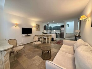 A modern living room with a sofa, dining table, and chairs, a kitchen with stainless steel appliances, and a flat-screen TV mounted on the wall. - B003 Superbe 2 chambres centre Cannes (Cannes)