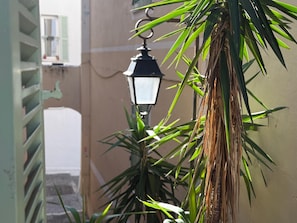 Een straatlamp met een hangende lamp, een palmboom en een gevel met een raam en luiken.