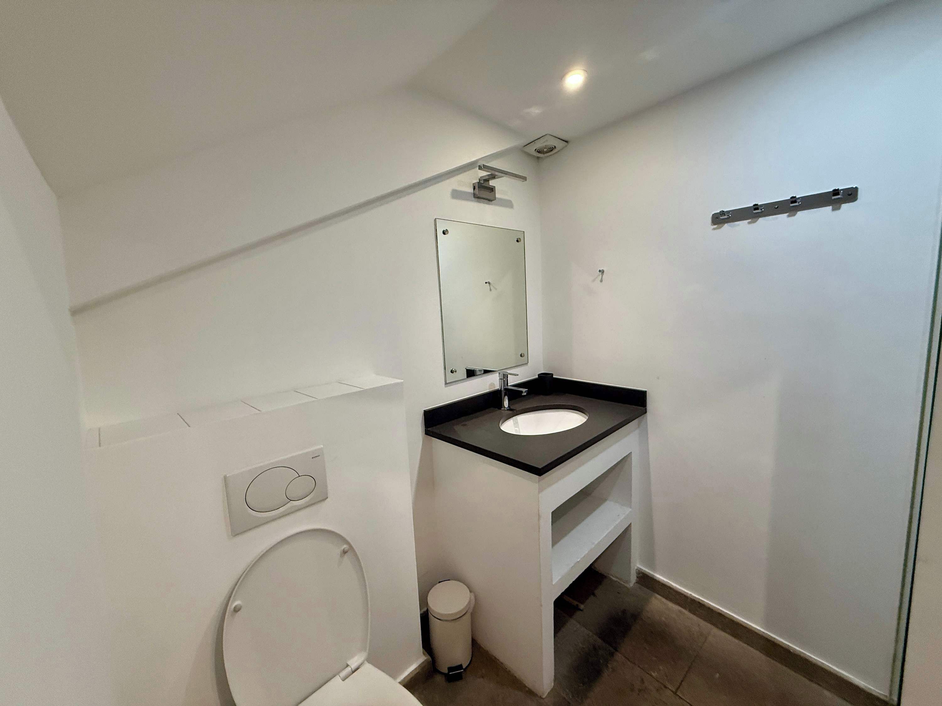Ein kleines, modernes Badezimmer mit Toilette, Waschbecken, Spiegel und Duschbereich.