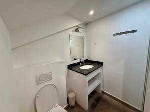 Un baño pequeño y moderno con inodoro, lavamanos, espejo y zona de ducha.