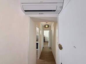 A hallway with a ceiling-mounted air conditioner, a door on the right, and a light fixture in the distance. - C033 Appartement fonctionnel au coeur du Suquet (Cannes)