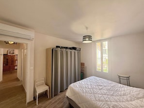 A bedroom with a bed, a chair, a wardrobe, a window, and a door leading to another room. - C033 Appartement fonctionnel au coeur du Suquet (Cannes)