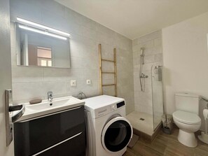 A modern bathroom with a sink, mirror, washing machine, toilet, and shower. - C033 Appartement fonctionnel au coeur du Suquet (Cannes)