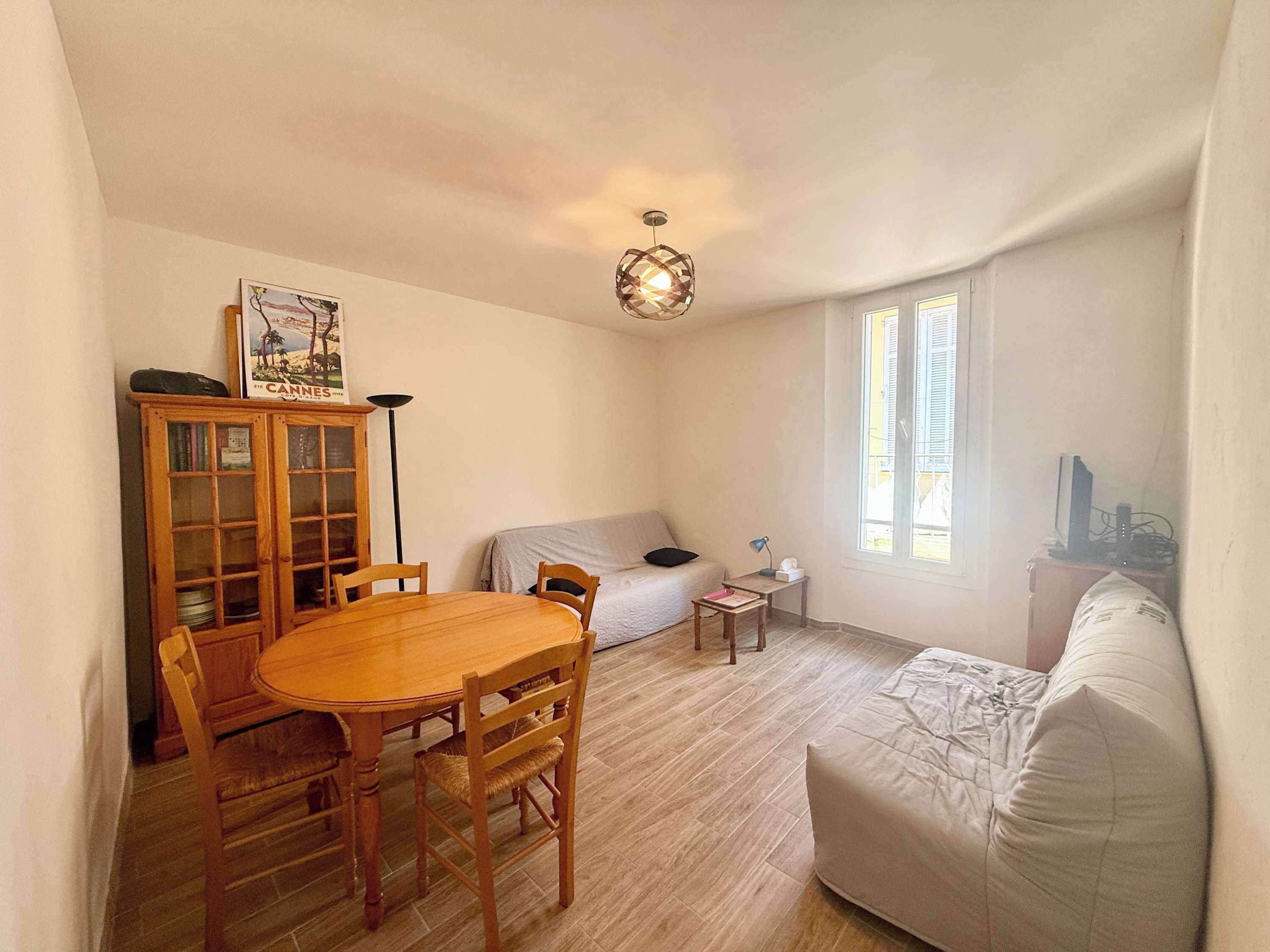 A compact living space with a dining table, chairs, a sofa, a small bedside table, and a lamp.