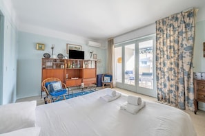 A hotel room with a bed, a seating area with a chair, a bookshelf, and a television. - A056 - Nice Studio Cannes centre with parking (Cannes)