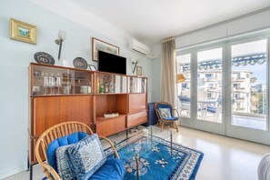 A living room with a large window, a wooden cabinet, a wicker chair, and a blue patterned rug. - A056 - Nice Studio Cannes centre with parking (Cannes)