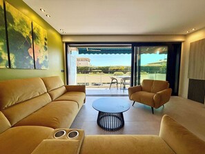 A modern living room with a sofa, armchair, and coffee table, a large window with a view of a balcony, and a painting on the wall. - B027 Magnifique 3 chambres parking, tout à pied (Cannes)