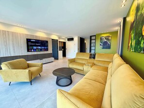 Un salon moderne avec un grand téléviseur à écran plat fixé au mur, un canapé d’angle et une table basse ronde.
