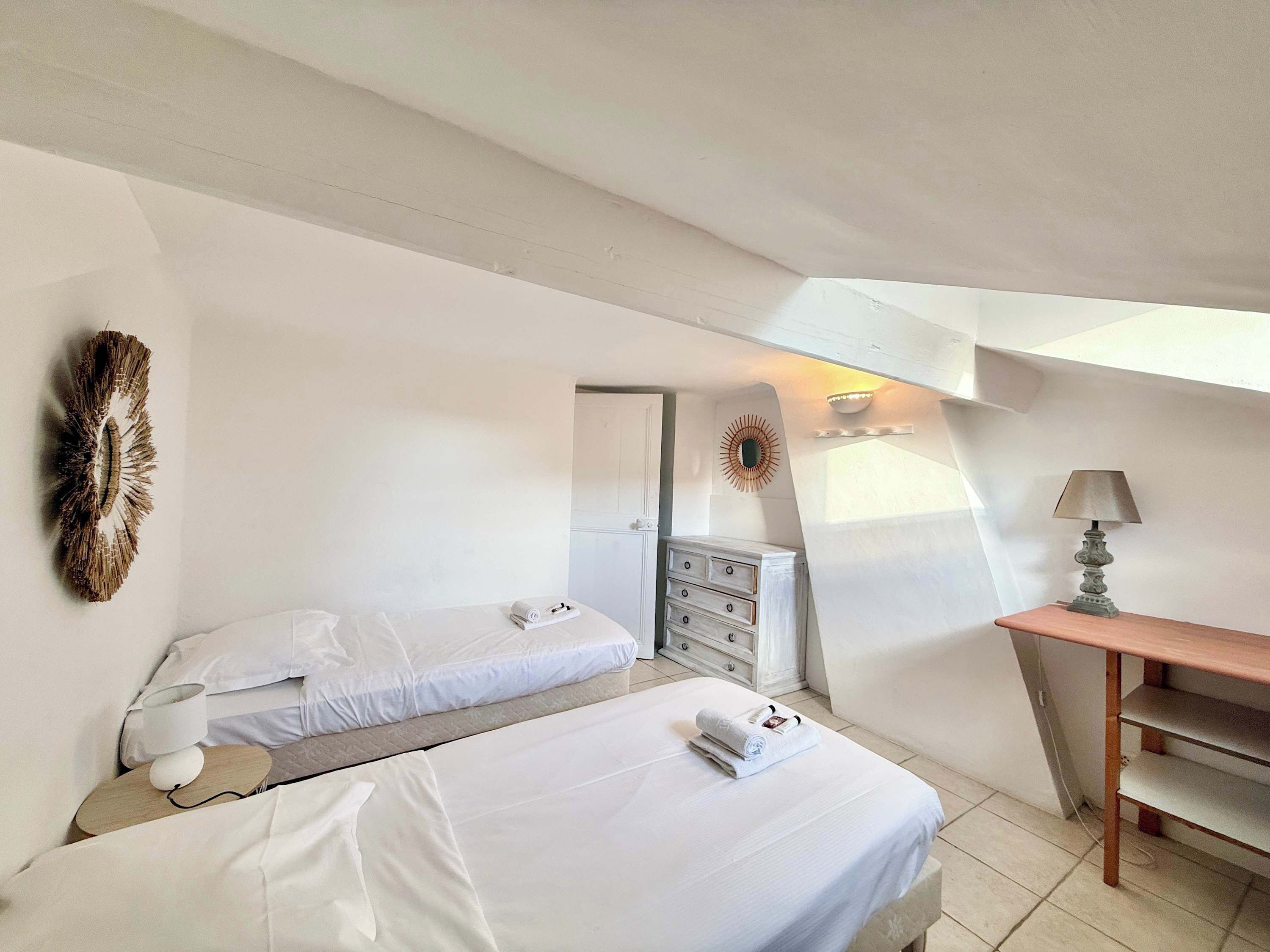 A bedroom with two beds, a dresser, a lamp, and a wall-mounted decor piece.