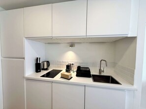 Et moderne køkken med hvide skabe, en sort induktionskogetop, elkedel, kaffemaskine og vask.