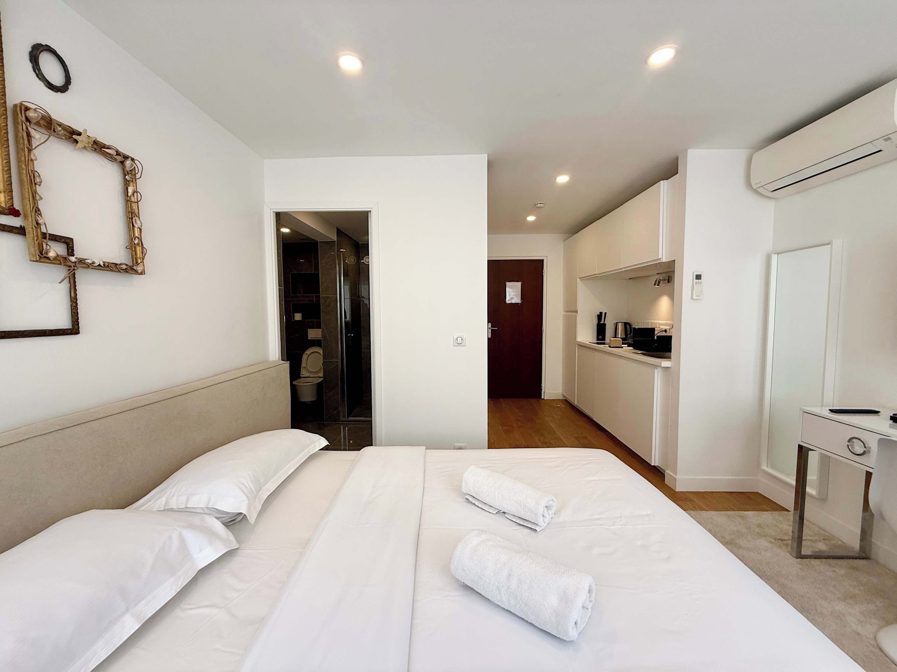 A hotel room with a bed, a small kitchenette, a bathroom, and a hallway.
