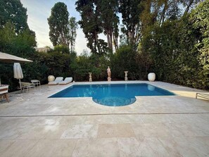 A swimming pool with a stone deck, surrounded by greenery and a statue. - B077 Superbe villa avec piscine centre de Cannes (Cannes)