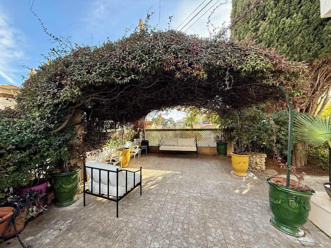 An outdoor patio area with a stone floor, a white bench, and potted plants.