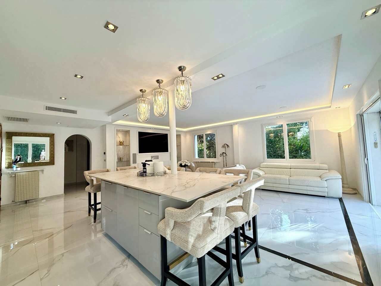 A spacious kitchen with a marble countertop, bar stools, and pendant lighting.