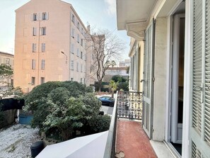 Un immeuble résidentiel doté d’un balcon, une voiture garée dans l’allée et une haie au premier plan.