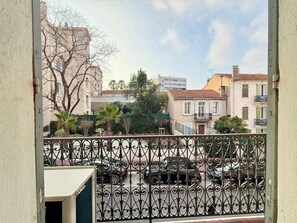 Un balcon doté d’une balustrade en fer forgé, donnant sur une rue bordée de voitures garées et d’immeubles.