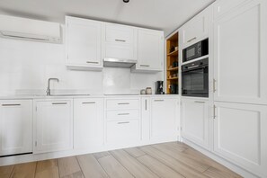 Moderni keittiö, jossa on valkoiset kaapit, sisäänrakennettu uuni ja kahvinkeitin.