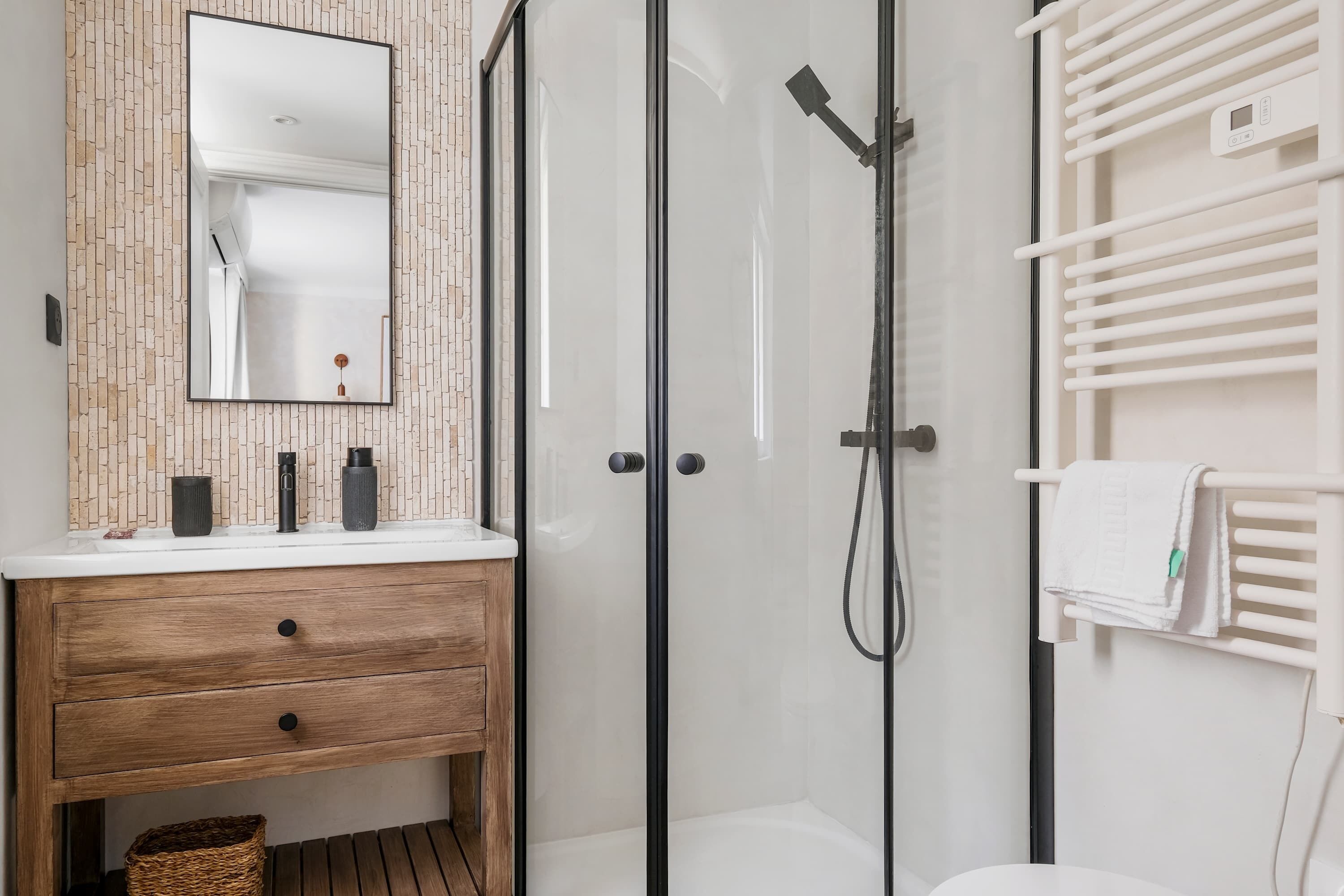 A modern bathroom with a wooden vanity, a glass shower enclosure, and a white towel rack.