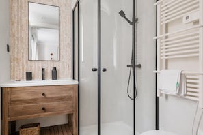 Um banheiro moderno com toucador de madeira, box de vidro e porta-toalhas branco.