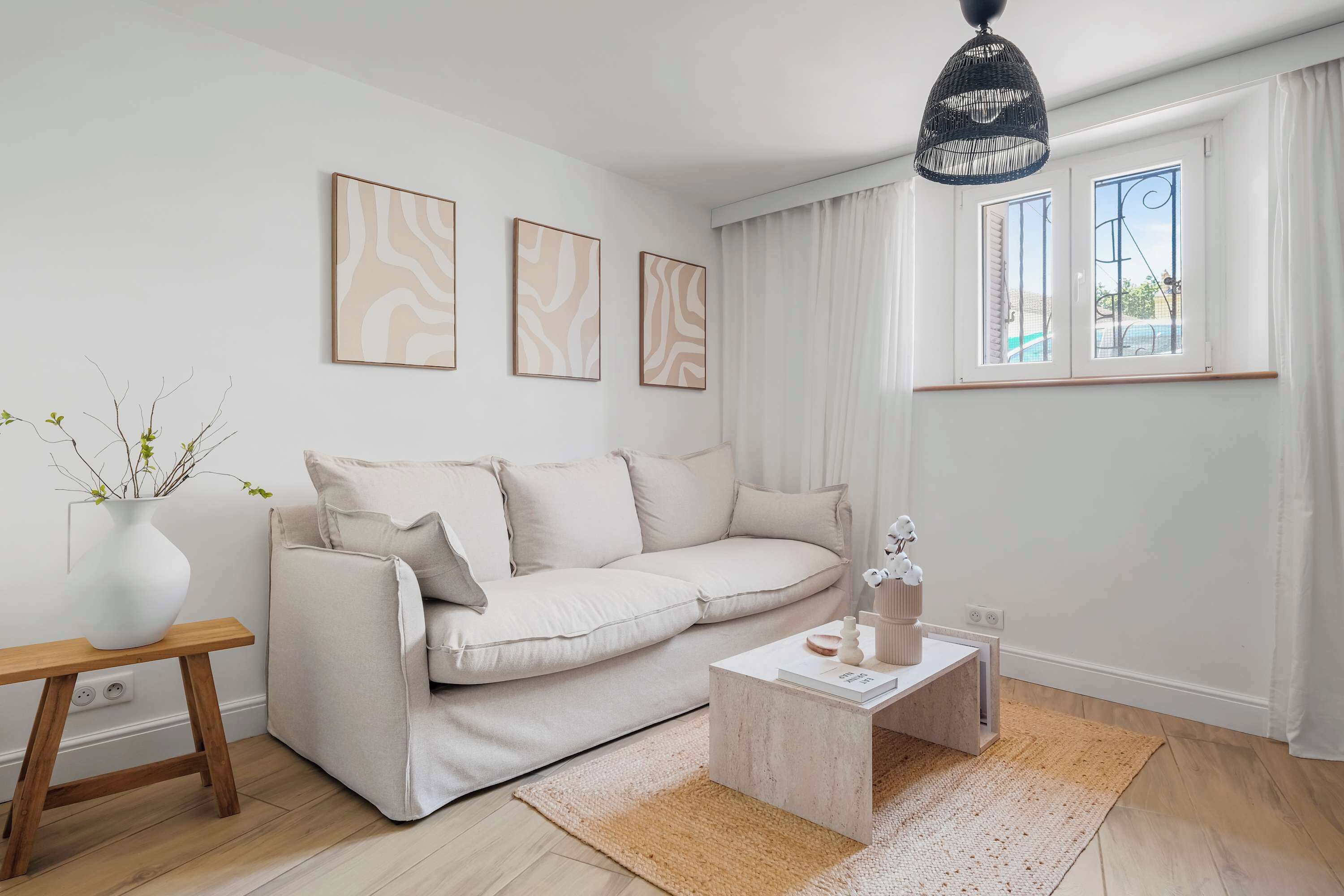 A minimalist living room with a white sofa, a coffee table, and a hanging light fixture.