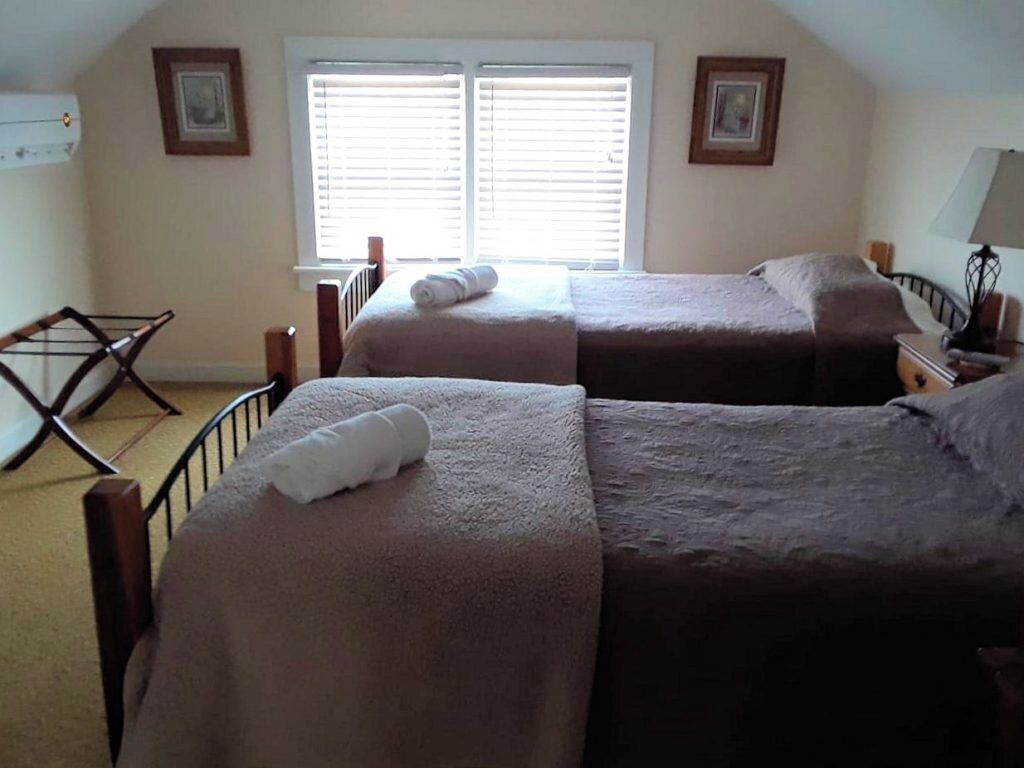 A bedroom with two beds, a window with blinds, a radiator, and a chair.