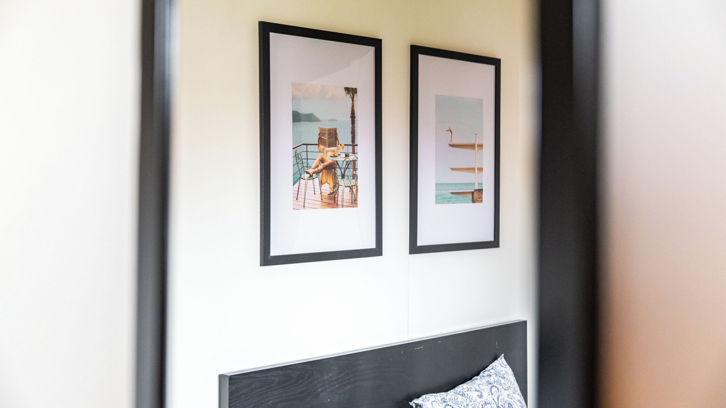 Two framed pictures on a wall, one depicting a beach scene and the other a coastal view with a boat.