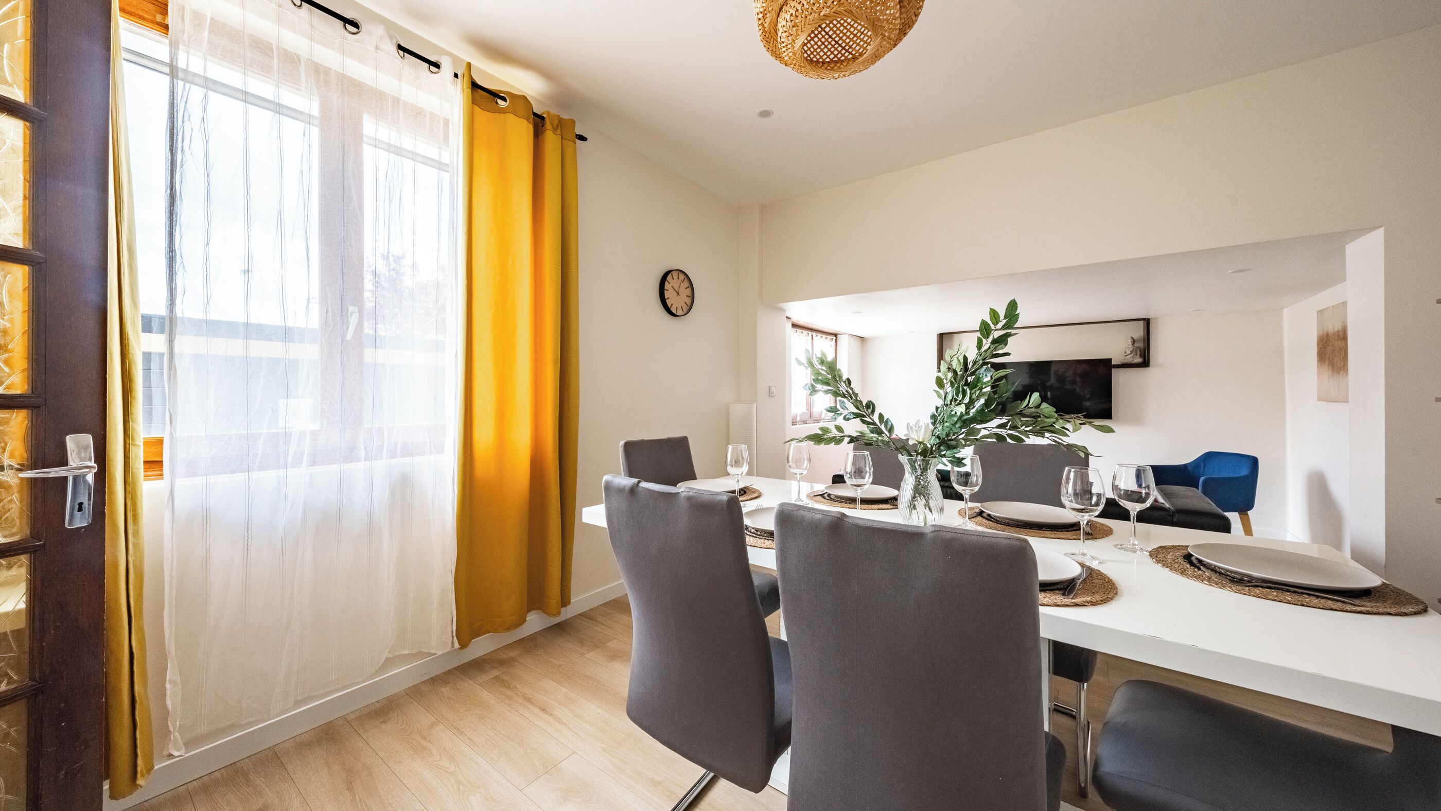 Un coin repas avec une table blanche, des chaises grises et un vase agrémenté de plantes vertes.