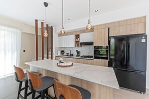 A modern kitchen with a central island, bar stools, a black refrigerator, and pendant lighting. - Villa in Punta Cana Downtown w/ Private pool and BBQ, Artificial Beach, Golf. (Punta Cana)