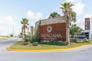 A sign for Vistacana with a logo, located at a street corner with palm trees and a modern building in the background. - Villa in Punta Cana Downtown w/ Private pool and BBQ, Artificial Beach, Golf. (Punta Cana)
