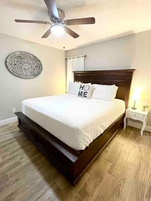 A bedroom with a bed, a ceiling fan, a wall decoration, a nightstand, and a lamp.