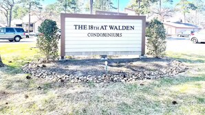 A sign for 'The 18th at Walden Condominiums' with a clear view of the surrounding area including trees and parked cars. - Cozy 1-bedroom condo near Lake Conroe (Montgomery)
