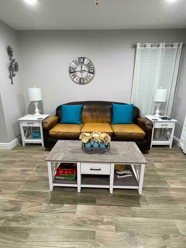 A living room with a brown sofa, two side tables, a coffee table with a vase, and a wall clock.