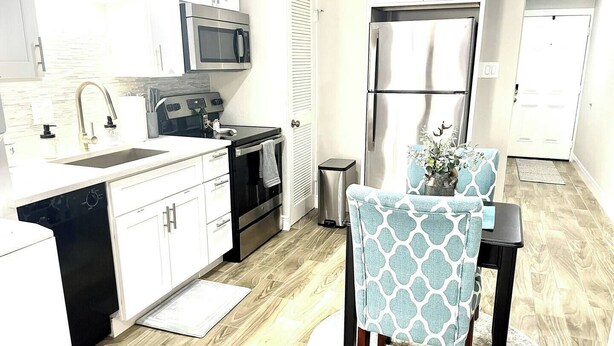 A modern kitchen with white cabinets, a stainless steel refrigerator, a microwave, and a dishwasher. There is a dining table with chairs and a small potted plant. - Cozy 1-bedroom condo near Lake Conroe (Montgomery)