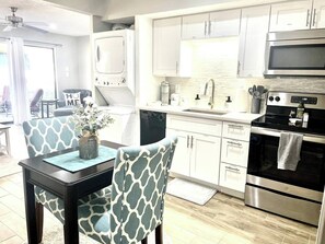 Una cocina moderna con armarios blancos, electrodomésticos de acero inoxidable y un comedor con sillas estampadas.