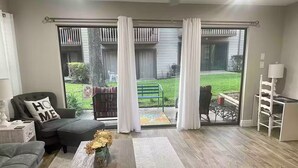 A living room with a grey sofa, a coffee table, and a view of a backyard through a sliding glass door. - Cozy 1-bedroom condo near Lake Conroe (Montgomery)